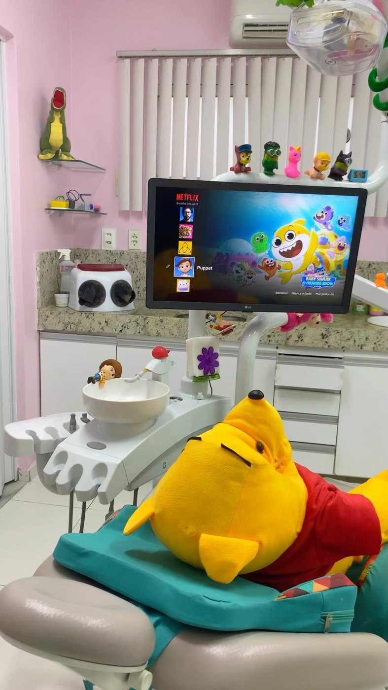 Pooh deitado na cadeira odontológica simulando um paciente, com TV ligada no Netflix