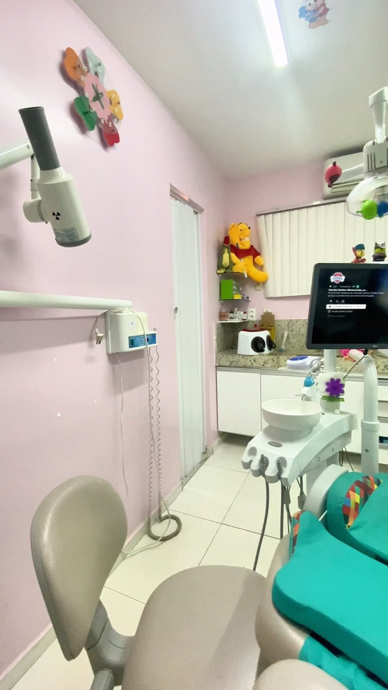 Consultório da Soma Odonto: parede rosa, cadeira odontológica turquesa e personagens infantis